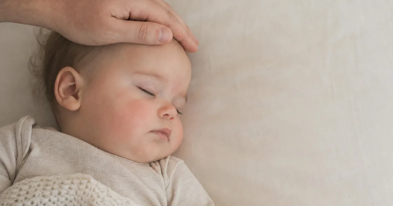 A parent resting a hand on their sleeping baby's forehead