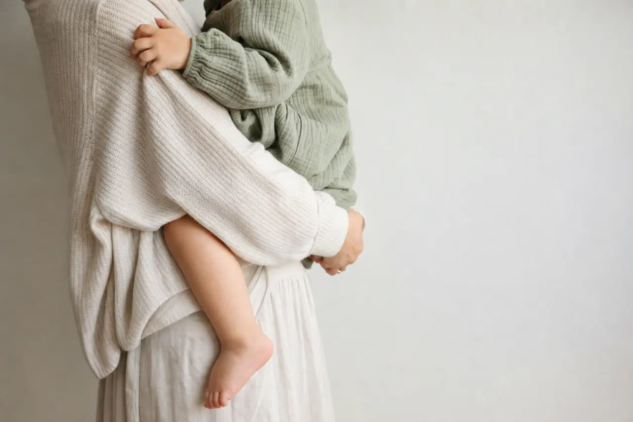 A parent holding a toddler on their hip at home