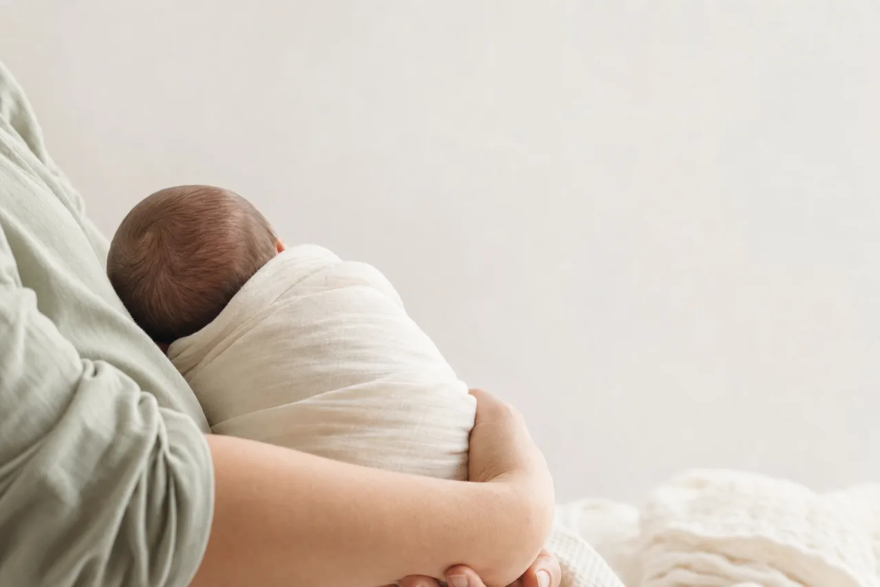 A swaddled newborn resting in a parent's arms